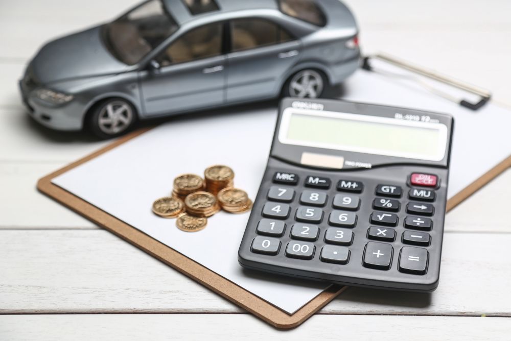 Model car, calculator, coins, and clipboard on a white table, representing car expenses or auto finance calculations—perfect for illustrating What Affects Your Car Scrap Value in Singapore.